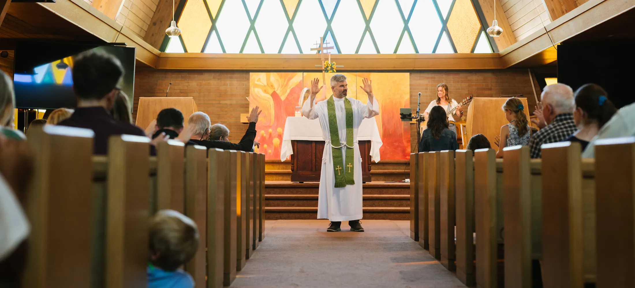 Looking up the center aisle during Sunday worship, with the congregation in the pews and the priest at the front beneath tall stained-glass windows