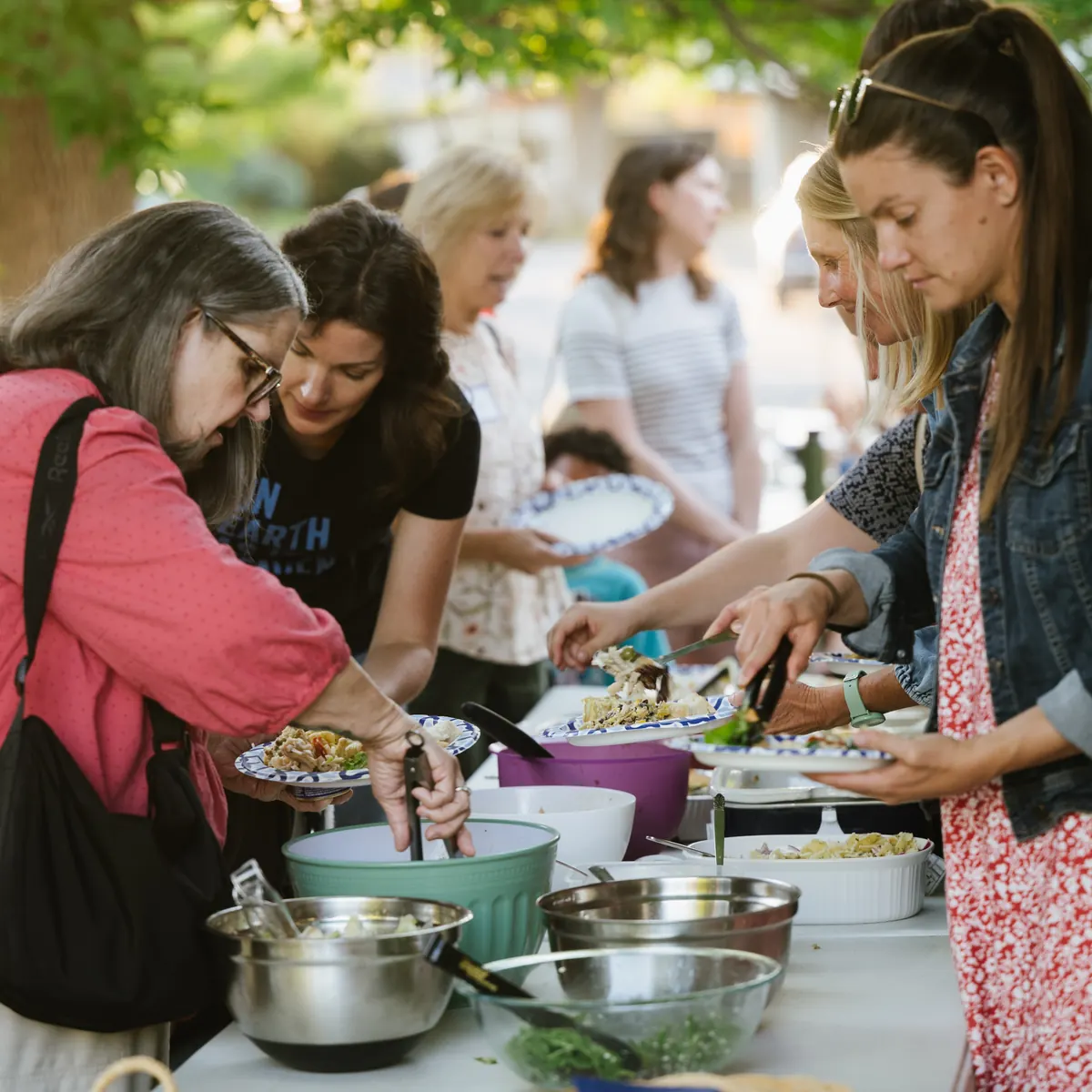 Church members of all ages serve themselves from a shared potluck table outdoors