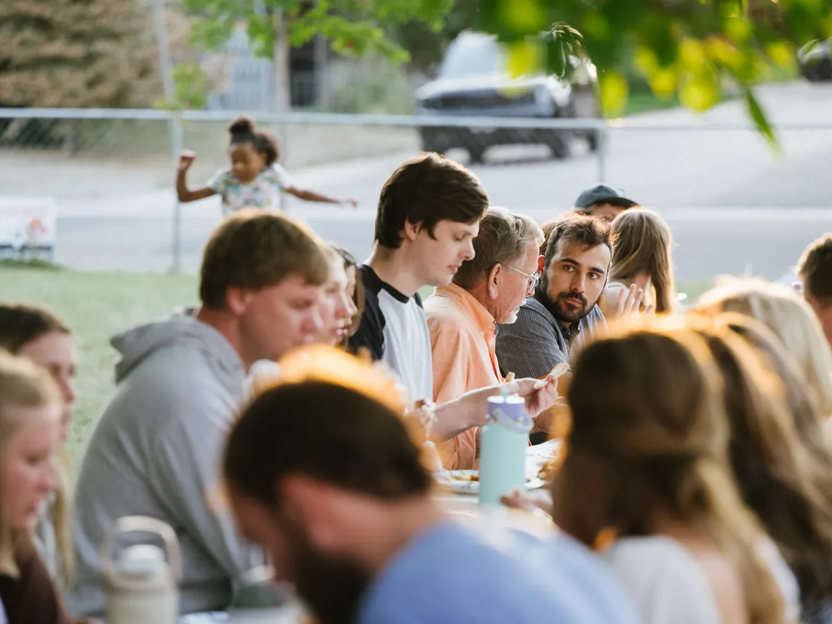 The congregation eating together at long tables outdoors on a summer evening